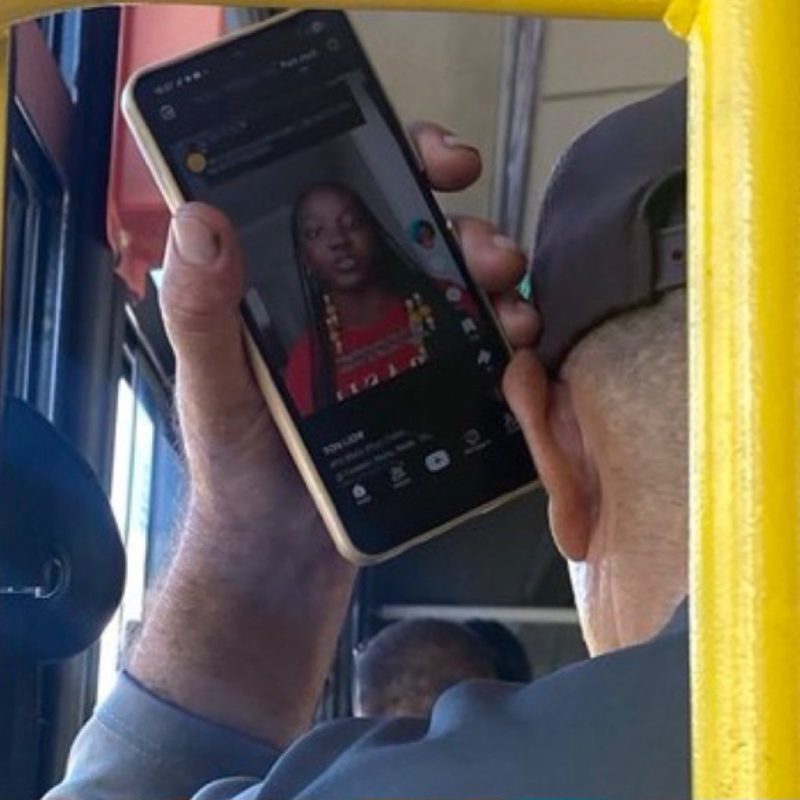 Homem de boné assistindo a um vídeo de campanha no celular, dentro de um ônibus